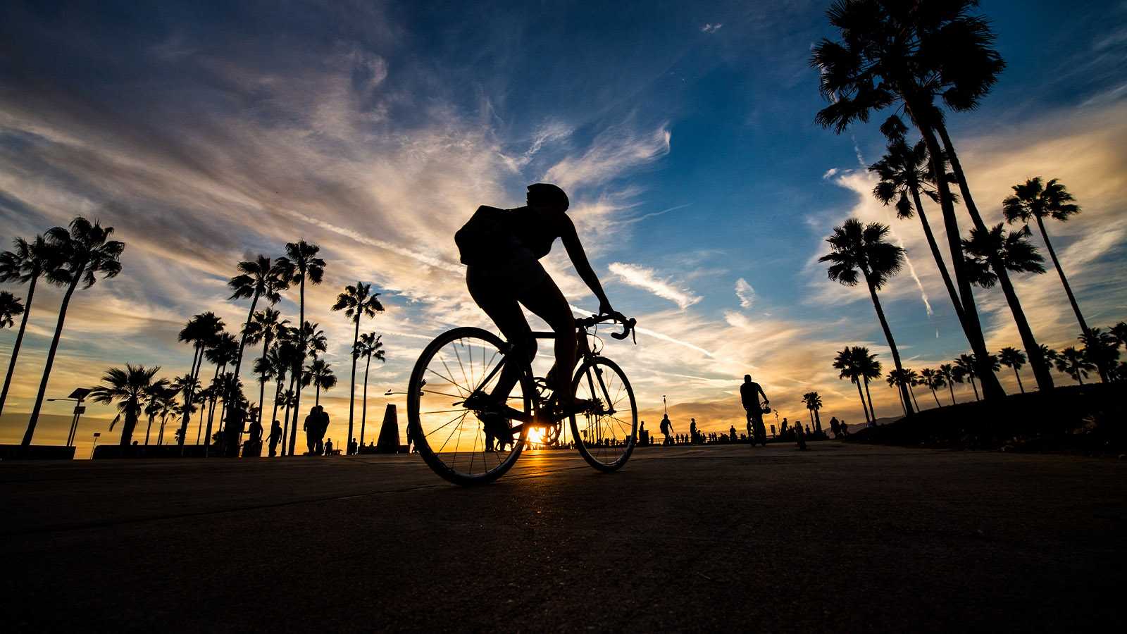 Urban bike rider follows path along coastal beaches during sunset